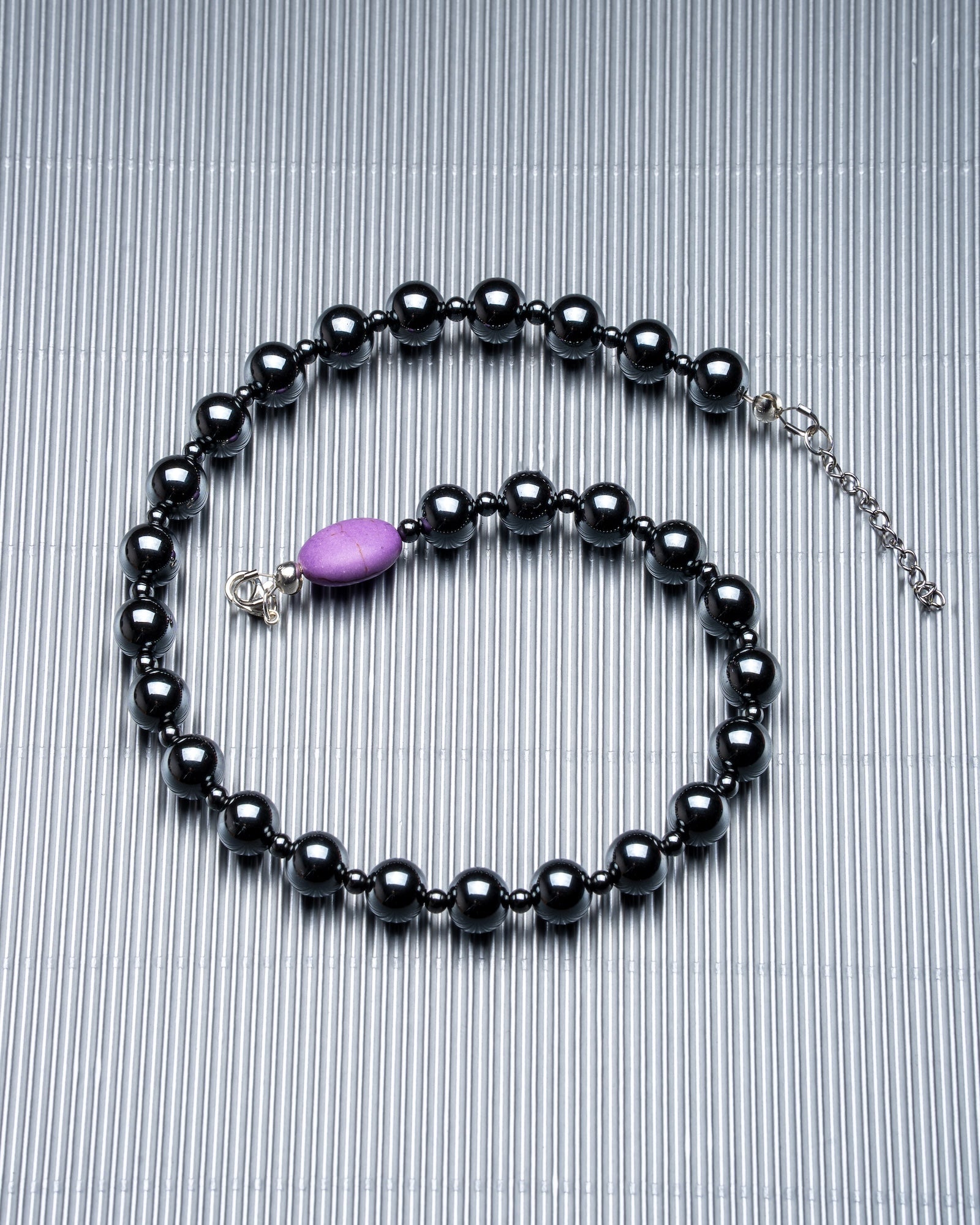 Unisex dark gray beaded gemstone necklace with a purple bead on a textured background