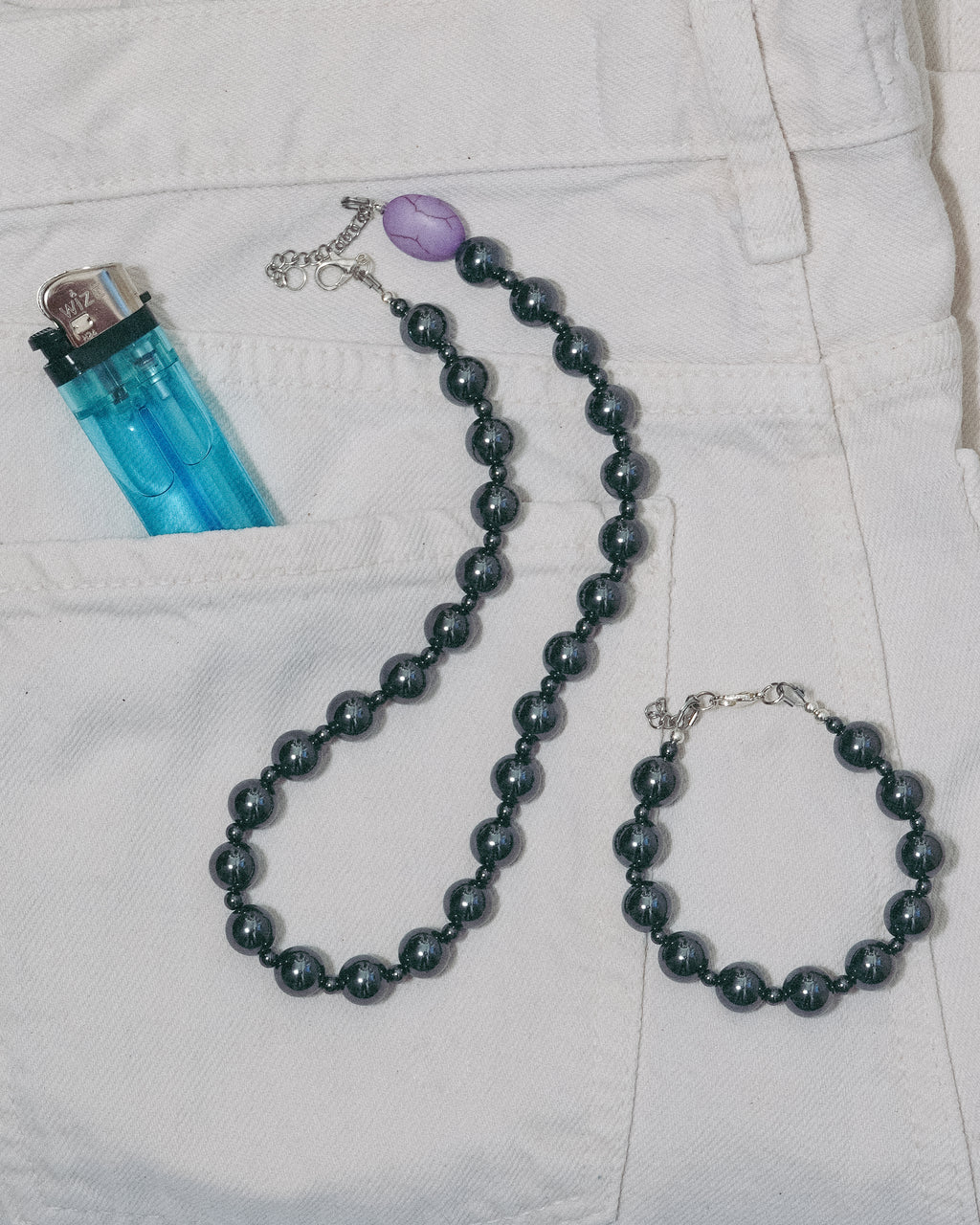 Unisex dark gray gemstone  beaded necklace and bracelet on a white jean 