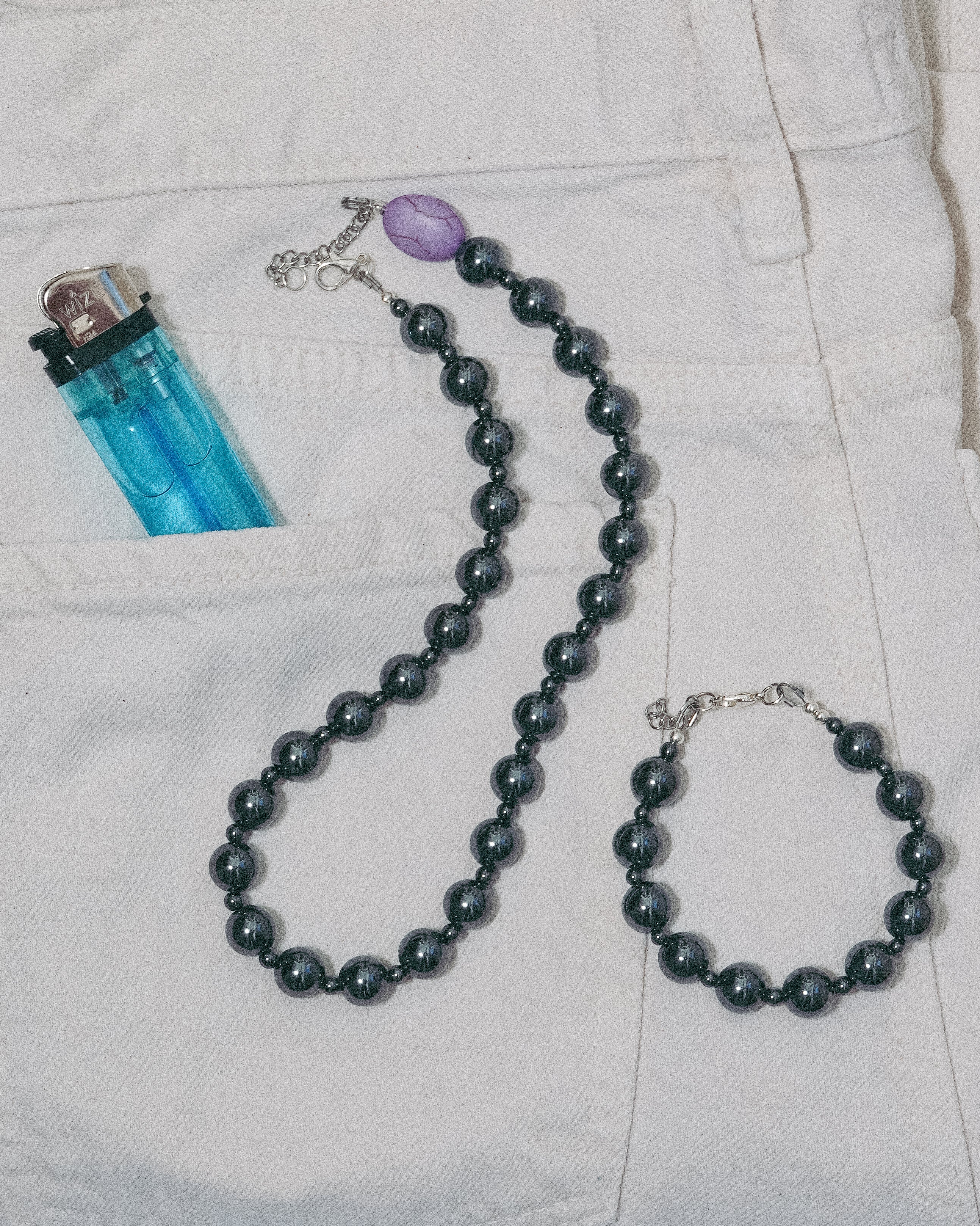 Unisex dark gray gemstone  beaded necklace and bracelet on a white jean 